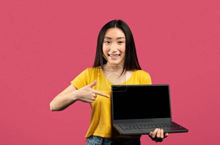Photo for Nice online offer. Happy korean lady shopping online, holding modern laptop, pointing at computer screen and smiling, posing on pink studio background, free space, mockup - Royalty Free Image
