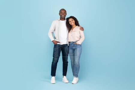 Téléchargez les photos : Portrait of happy black adult couple embracing, looking at camera and smiling while posing over blue studio wall, free space, full body length - en image libre de droit