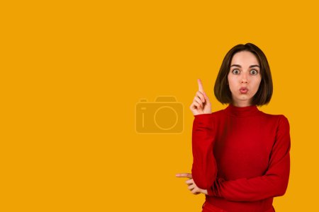 Foto de Excited beautiful brunette young lady with nice hairstyle in red showing eureka gesture and grimacing on orange studio background, inspired woman having nice idea, copy space - Imagen libre de derechos