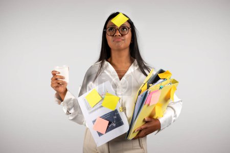 Foto de Busy tired young black business woman in glasses with many folders with cup coffee takeaway look at sticker on forehead isolated on white background, studio. Multitasking, deadline for work, business - Imagen libre de derechos
