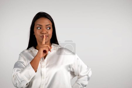 Photo for Pensive young african american business woman presses finger to lips, making shhh sign, looks at empty space, isolated on white background, studio, close up. Secret gesture for work, business, startup - Royalty Free Image