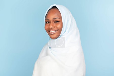Téléchargez les photos : Portrait of beautiful black muslim woman in hijab posing on blue studio background, smiling at camera, copy space. Feminine beauty concept, women diversity - en image libre de droit