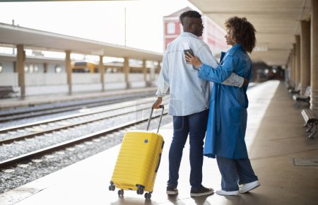 Foto de Romantic Black Couple Standing On Platform At Railway Station And Embracing, Loving African American Man And Woman Carrying Suitcase And Hugging While Waiting For Train On Platform, Copy Space - Imagen libre de derechos