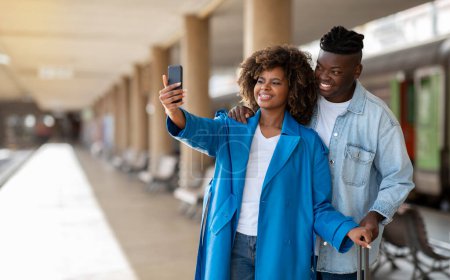 Téléchargez les photos : Happy Travellers. Young Black Couple With Smartphone Taking Selfie At Railway Station, Cheerful African American Spouses Standing On Platform And Making Photos While Waiting Train, Copy Space - en image libre de droit