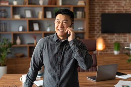 Photo for Smiling confident mature chinese guy call by phone, has business conversation in office interior. Success, great deal, technology for work and communicating remotely, new normal and talk with client - Royalty Free Image