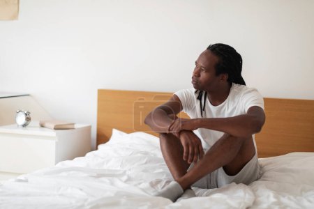 Photo for Portrait Of Pensive Young Black Male Sitting On Bed And Looking Away, Thoughtful Millennial African American Guy Resting At Home In Bedroom Interior, Thinking About Life Problems, Copy Space - Royalty Free Image