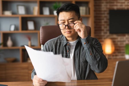 Foto de Serious concentrated mature japanese man boss in glasses works with documents at workplace in office interior. Trading, modern business remotely, financial data analysis for startup, new contract - Imagen libre de derechos