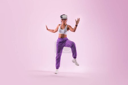 Téléchargez les photos : Young black woman dancing in the metaverse, having fun while wearing virtual reality goggles, pink studio background, neon light. Lady exploring 3D technology - en image libre de droit