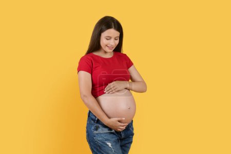 Téléchargez les photos : Maternity Concept. Portrait Of Beautiful Smiling Pregnant Woman Caressing Her Belly While Standing Isolated Over Yellow Background, Happy Expectant Lady Enjoying Upcoming Motherhood, Copy Space - en image libre de droit