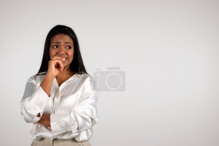 Téléchargez les photos : Sad confused young african american business woman biting her finger, suffering from pressure, stress, look at free space isolated on white background, studio. Problems with work, business, deadline - en image libre de droit