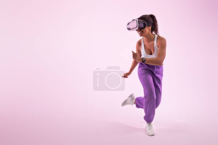Foto de Experiencing the metaverse. Active african american lady gaming with virtual reality goggles over pink background, free space. Young woman enjoying 3D experience in studio - Imagen libre de derechos