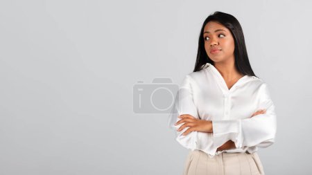 Téléchargez les photos : Serious thoughtful millennial black lady in white blouse thinking, creating idea for startup, looking at empty space, isolated on gray background, studio. Business solution, work, study, ad and offer - en image libre de droit