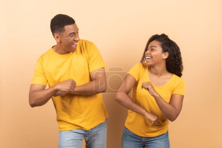 Téléchargez les photos : Enjoying life. Happy carefree black spouses dancing and having fun, looking at each other and smiling over yellow studio background, copy space - en image libre de droit