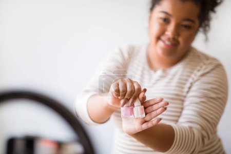 Téléchargez les photos : Closeup of hispanic millennial chubby woman in casual outfit streaming from home, using pro blogger set and smartphone, showing brand new nail polisher, influencer promoting cosmetics, copy space - en image libre de droit