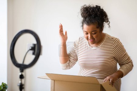 Photo for Excited emotional happy overweight young woman with curly hair famous blogger opening paper box parcel in front of camera, lady smiling and gesturing while looking inside package - Royalty Free Image