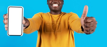 Photo for Mobile Ad. Smiling Black Guy Demonstrating Blank Smartphone And Showing Thumb Up At Camera, Unrecognizable African American Man Recommending New Application Or Website, Collage, Mockup - Royalty Free Image