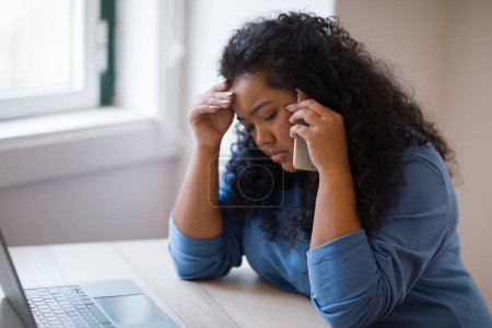 Photo for Upset hispanic curly overweight young lady sitting at workdesk, working online on laptop pc computer on table, businesswoman having phone conversation and touching head, side view, copy space - Royalty Free Image