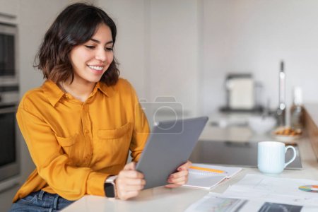Téléchargez les photos : Remote Education. Smiling Young Arab Woman Study With Digital Tablet In Kitchen, Happy Middle Eastern Female Using Modern Gadget At Home For Online Lesson, Enjoying Distance Learning, Copy Space - en image libre de droit