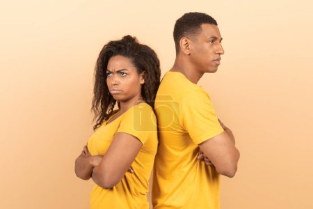 Foto de Relationship crisis. Offended black spouses standing back to back over yellow background, ignoring each other after argue, suffering marriage problems - Imagen libre de derechos