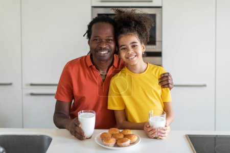 Photo for Portrait Of Cheerful Young Black Father And Preteen Daughter Posing In Kitchen While Eating Snacks Together, Happy African American Dad And Female Child Having Muffins And Milk For Lunch - Royalty Free Image