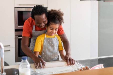Photo for Cheerful black dad and preteen daughter rolling dough while baking together in kitchen, happy african american family father and female child wearing aprons cooking pastry at home, copy space - Royalty Free Image