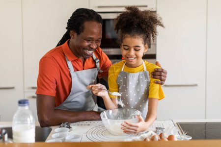 Téléchargez les photos : Home Bakers. Cheerful Black Dad And Preteen Daughter Baking Together In Kitchen, Happy African American Father And Female Child Preparing Dough For Pastry, Girl Adding Flour To Bowl, Free Space - en image libre de droit