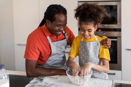 Téléchargez les photos : Black girl and her father kneading dough while baking in kitchen, happy african american man and his female child cooking at home, enjoying making homemade pastry, closeup shot with free space - en image libre de droit