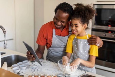 Photo for Black Father Using Digital Tablet While Baking With Daughter At Home, Happy African American Dad And Preteen Female Child Checking Muffins Recipe Online, Enjoying Cooking Pastry Together, Free Space - Royalty Free Image