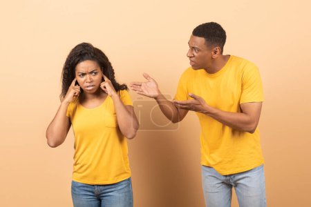 Foto de Conflict, family relationship problems. Angry black man screaming at wife, mad woman covering ears with hands isolated on yellow studio background - Imagen libre de derechos