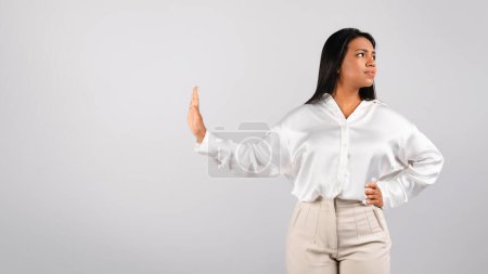 Foto de Serious confident millennial black female in white blouse looking away, doing stop gesture with hand, isolated on gray background, studio. Personal space sign for business, work, bad deal and say no - Imagen libre de derechos