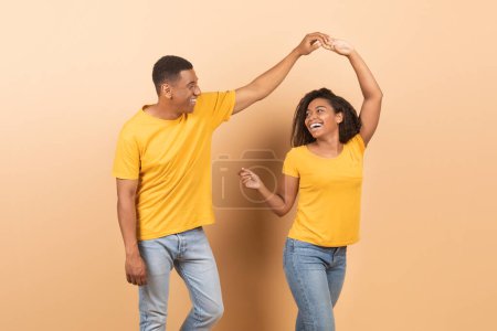 Téléchargez les photos : Cheerful african american couple dancing over yellow background, happy romantic black spouses having fun together, holding hands and smiling, banner - en image libre de droit