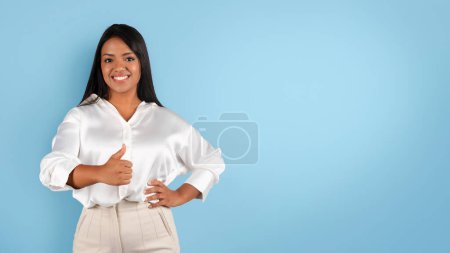 Téléchargez les photos : Glad confident millennial black female in white blouse show thumb up, isolated on blue background, studio, panorama. Recommendation, advice from professional, great deal, business, work and study - en image libre de droit