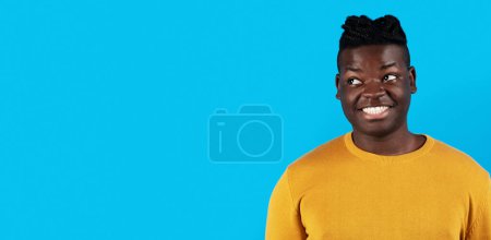 Téléchargez les photos : Portrait Of Smiling Young Black Man Looking Aside At Copy Space With Interest, Curious Pensive Millennial African American Male Standing Isolated Over Blue Studio Background, Panorama - en image libre de droit