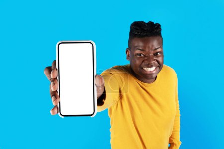 Téléchargez les photos : Check This. Cheerful Black Man Demonstrating Smartphone With Blank White Screen In Hand, Happy African American Guy Recommending Mobile Offer Or Website While Standing On Blue Background, Mockup - en image libre de droit