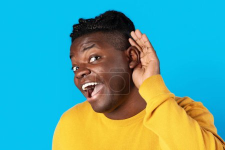 Téléchargez les photos : Curious Cheerful Black Man Holding Hand Near Ear Trying To Overhear Something, Excited Young African American Guy Interested In Fresh Gossips, Posing Isolated On Blue Background, Closeup - en image libre de droit