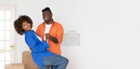 Téléchargez les photos : Happy Young Black Spouses Dancing Together In Bright Room While Moving Home, Cheerful African American Couple Celebrating Relocation To New Flat, Making Dance Among Unpacked Cardboard Boxes - en image libre de droit