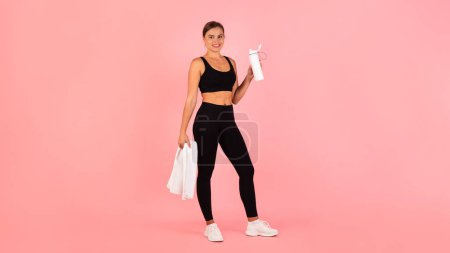 Téléchargez les photos : Young Sporty Woman In Activewear Holding Fitness Bottle With Water And, Athletic Millennial Female Posing After Sport Workout, Standing Over Pink Studio Background, Panorama With Copy Space - en image libre de droit