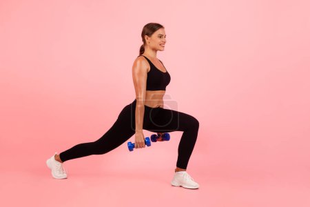 Téléchargez les photos : Sporty Young Woman Holding Dumbbells And Making Deep Lunges Exercise Over Pink Background In Studio, Athletic Female In Sportswear Training Legs, Fit Lady Doing Bodybuilding Workout, Copy Space - en image libre de droit