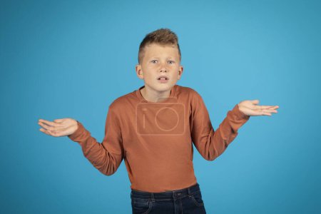 Téléchargez les photos : I Dont Know. Doubtful Preteen Boy Shrugging Shoulders And Spreading Arms, Portrait Of Doubtful Kid Looking At Camera, Unsure Male Child Standing Isolated Over Blue Studio Background, Copy Space - en image libre de droit