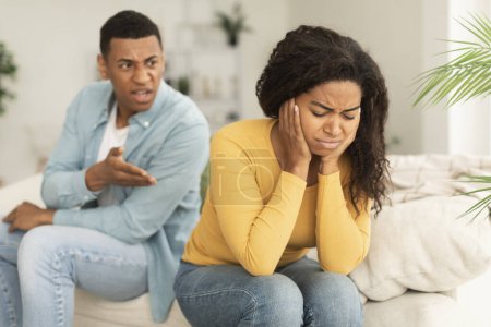 Photo for Sad crying young african american woman ignores angry aggressive screaming guy sit on sofa, think about breakup in room interior. Scandal quarrel, relationship problems, crisis and divorce at home - Royalty Free Image