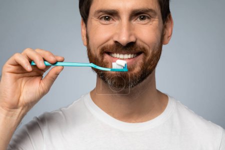 Téléchargez les photos : Happy caucasian man cleaning teeth with toothbrush and smiling, standing over grey studio background. Healthy teeth, toothcare hygiene routine concept - en image libre de droit