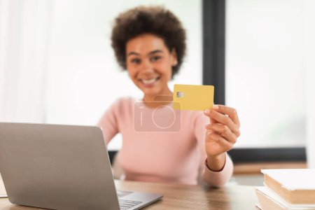 Foto de Glad young mixed race woman manager show credit card use laptop, checks finances on bank account, recommend saving in office interior, blurred. Work, business remotely, online shopping, huge sale - Imagen libre de derechos