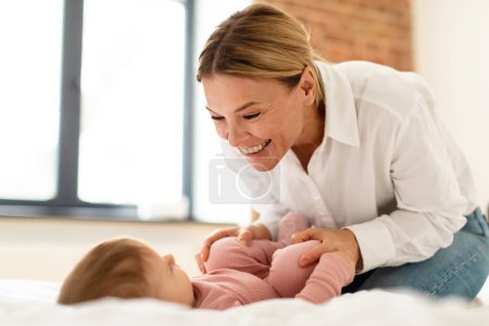 Téléchargez les photos : Child care concept. Happy mother making gymnastics to her newborn baby, bonding with infant while spending time together in bedroom, free space - en image libre de droit