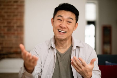 Photo for Hello. Portrait of happy mature asian man gesturing and talking at camera, sitting on sofa at home. Positive japanese male having video call. Modern remote communication - Royalty Free Image