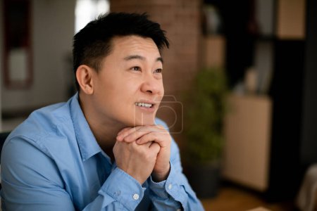 Photo for Dreamy middle aged asian businessman thinking of new business strategy, sitting at home office, looking aside and smiling, free space. Portrait of mature korean male entrepreneur - Royalty Free Image