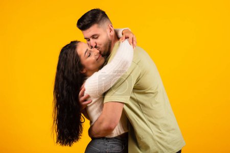 Photo for Satisfied handsome millennial middle eastern man hugging and kissing female, couple enjoy free time and tender moment date isolated on orange background, studio. Family relationships, love and romance - Royalty Free Image