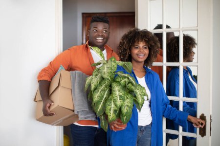 Foto de Excited black couple entering their apartment and carrying boxes with belongings, amazed african american spouses walking in new home, standing in doorway of modern flat, looking at interior together - Imagen libre de derechos