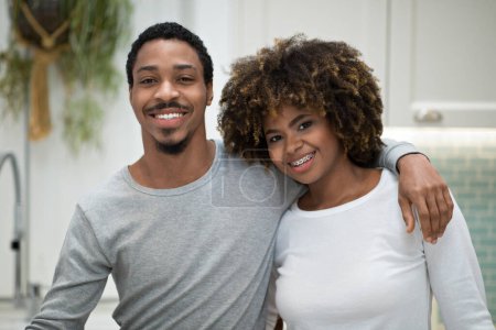 Foto de Happy Marriage. Joyful African American Husband Hugging Wife Smiling Looking At Camera Standing At Home. Happy Young Couple Embracing Posing Together At Kitchen. Love And Romantic Relationship Concept - Imagen libre de derechos