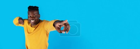 Téléchargez les photos : Big Sale. Excited Young Black Man Pointing Away With Two Hands While Standing Isolated Over Blue Studio Background, Cheerful African American Male Demonstrating Copy Space For Advertisement, Panorama - en image libre de droit