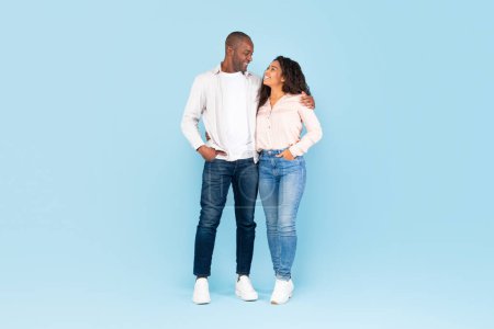 Photo for Full length shot portrait of black couple hugging and looking at each other, posing over blue studio background, full body length, free space - Royalty Free Image